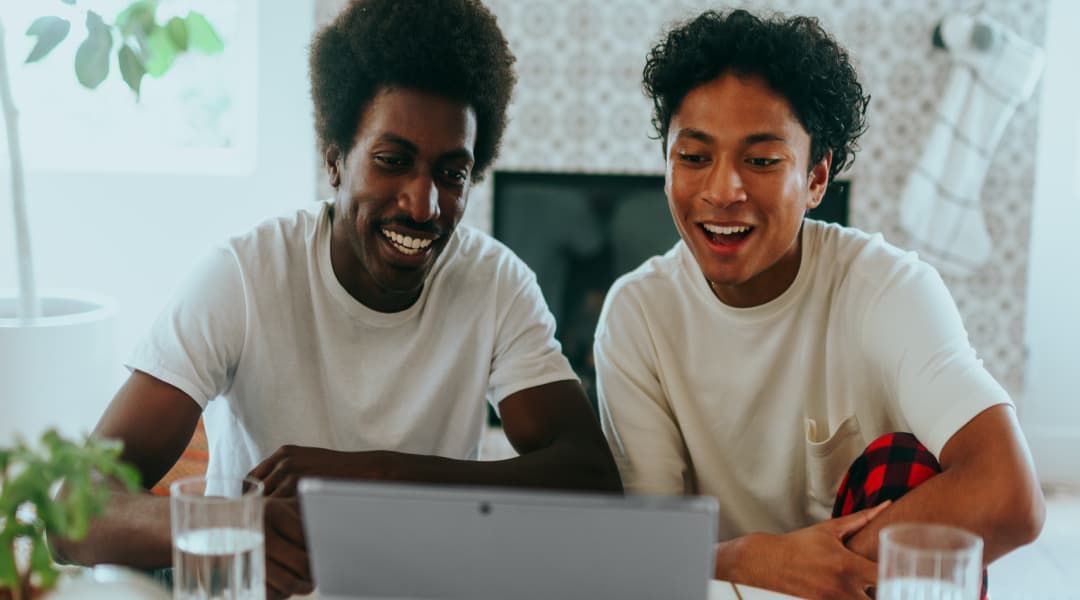 two people laughing while using a laptop