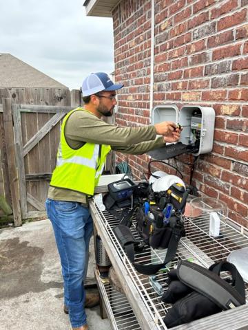 A technician on a working outside by a brick wall.